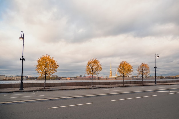Dramatischer Blick auf die Herbststadt. Gelbe Herbstbäume auf dem Granitdamm in St. Petersburg. Russland.