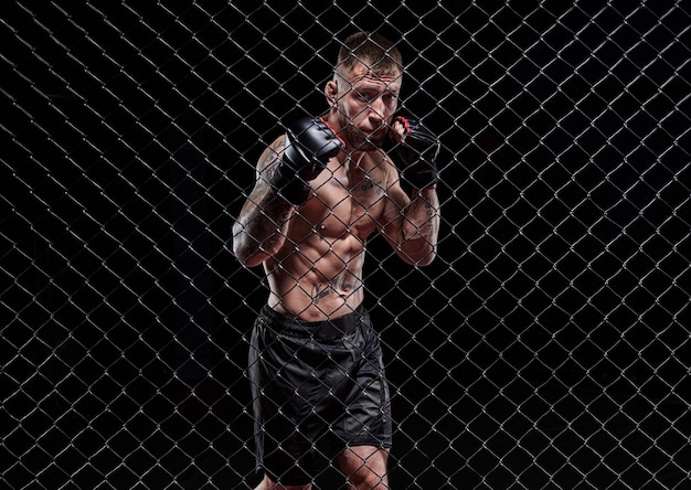Dramatisches Bild eines Mixed-Martial-Arts-Kämpfers, der in einem achteckigen Käfig steht Das Konzept der Sportbox-Kampfkünste