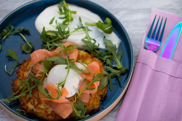 Draniki frito con pescado rojo salado y huevo escalfado Un plato decorado con hierbas y crema agria