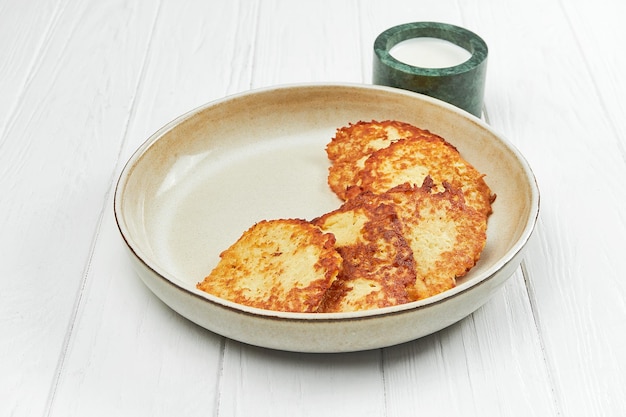 Draniki de patata ucraniana o croquetas de patata en un plato sobre un fondo de madera blanca