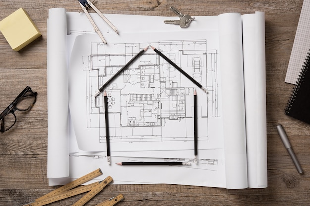 Draufsicht auf architektonische Blaupausen, Rollen und Zeicheninstrumente auf dem Arbeitstisch.