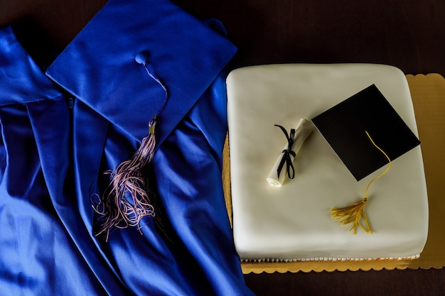 Draufsicht auf blaues Abschlusskleid und Mütze mit Kuchen zum Schulabschluss.