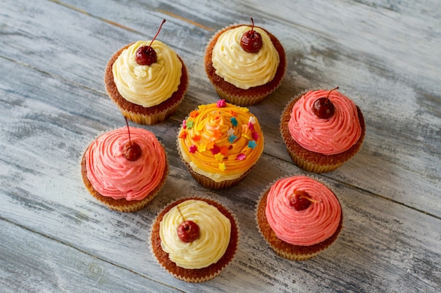 Draufsicht auf bunte Cupcakes-Desserts auf grauer Holzoberfläche, köstliches Gebäck mit Zuckerguss,...