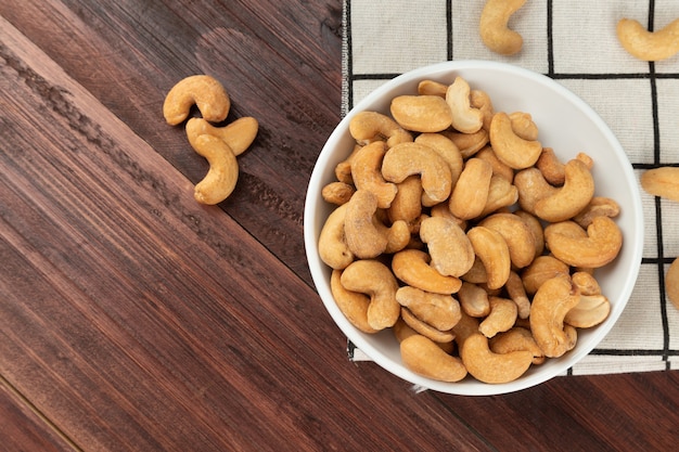 Draufsicht auf Cashewnüsse in weißer Schüssel auf dem Tisch, flache Lage, gesunder Snack, vegetarisches Essen.