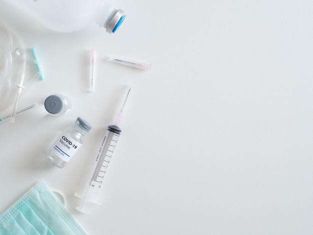 Draufsicht auf das Covid-19-Impfstoffkonzept mit Spritze, medizinischer Maske, Medizin und Reagenzglas