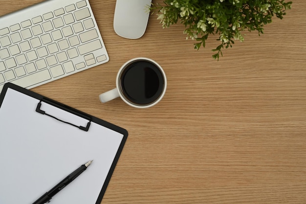 Draufsicht auf das Klemmbrett für eine Kaffeetasse mit kabelloser Tastatur und eine Topfpflanze auf einem hölzernen Schreibtisch