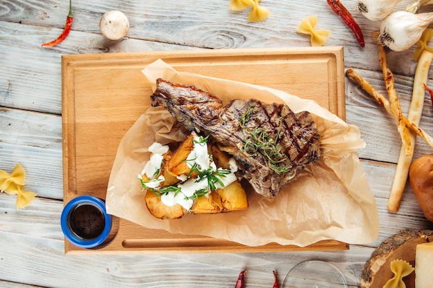 Draufsicht auf das t Knochensteak mit Kartoffeln in saurer Sahne auf dem Holzbrett