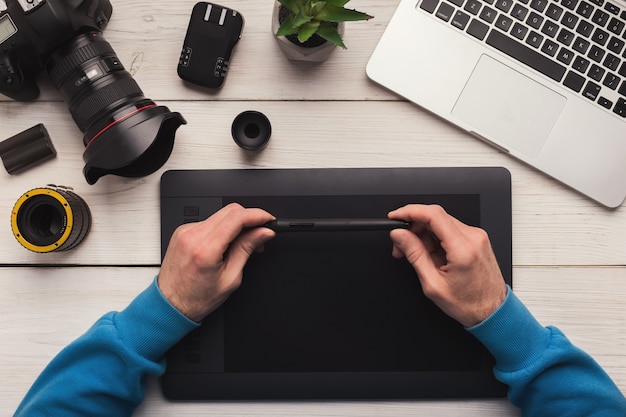 Draufsicht auf den Arbeitsplatz des Fotografen. Kreative Designerhände arbeiten mit Grafiktablett, Fotoausrüstung auf dem Tisch