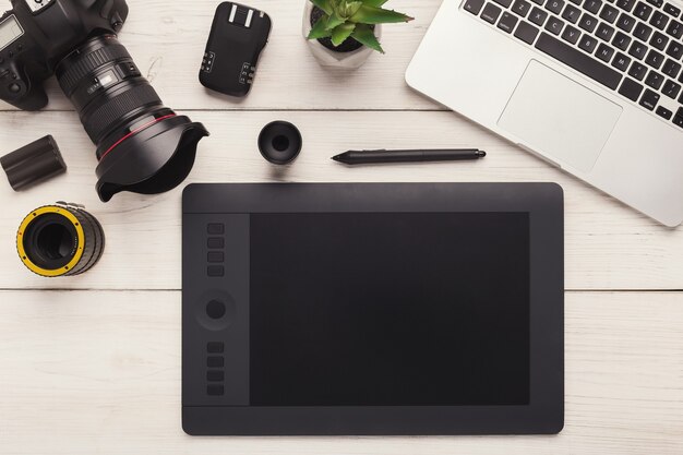 Draufsicht auf den Arbeitsplatz des Fotografen oder kreativen Designers. Schreibtisch mit Grafiktablett, Laptop, Kamera, Objektiv und anderer Fotoausrüstung, Kopierraum