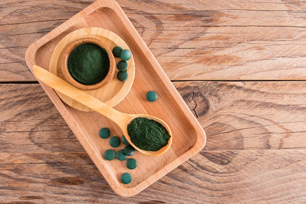 Draufsicht auf den Holztisch mit umweltfreundlichen Gerichten, die mit Spirulina-Algenpulver und grünen Tabletten als Lebensmittelzusatzstoff gefüllt sind