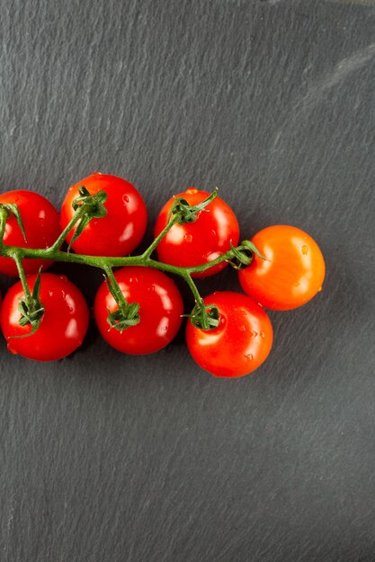 Draufsicht auf den nassen frischen Kirschtomatenzweig, der auf der glatten Oberfläche des schwarzen Schiefers liegt