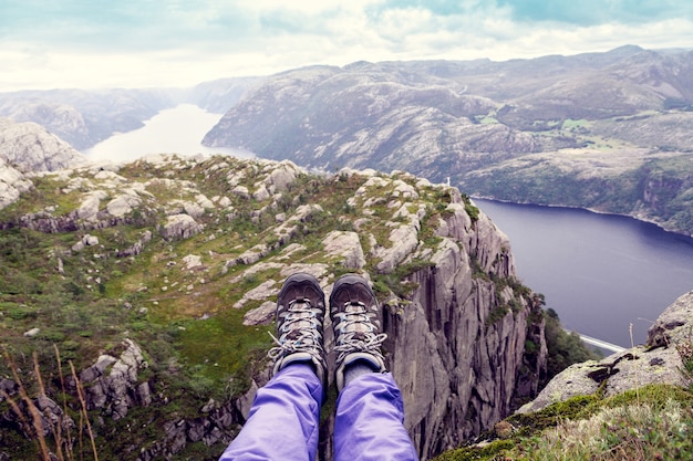 Draufsicht auf den norwegischen Fjord mit Touristenbeinen im Vordergrund
