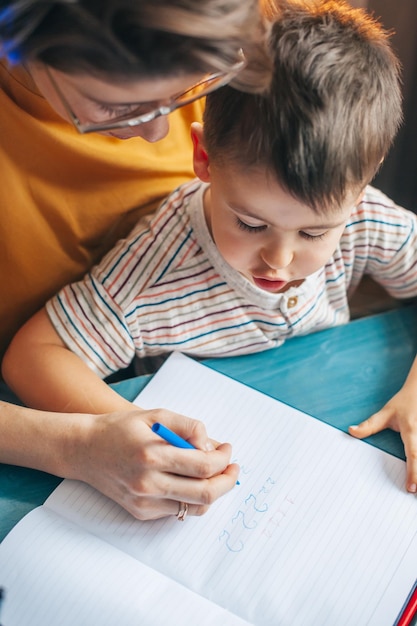 Draufsicht auf die Hände von Mutter und Sohn, die Zahlen für die Familienschule schreiben