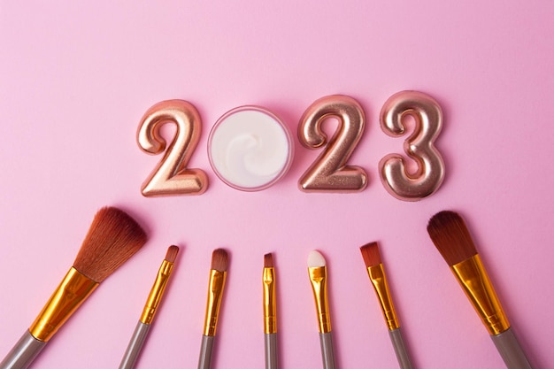 Draufsicht auf die Make-up-Pinsel auf rosa HintergrundRoségoldene Zahlen 2023 oben