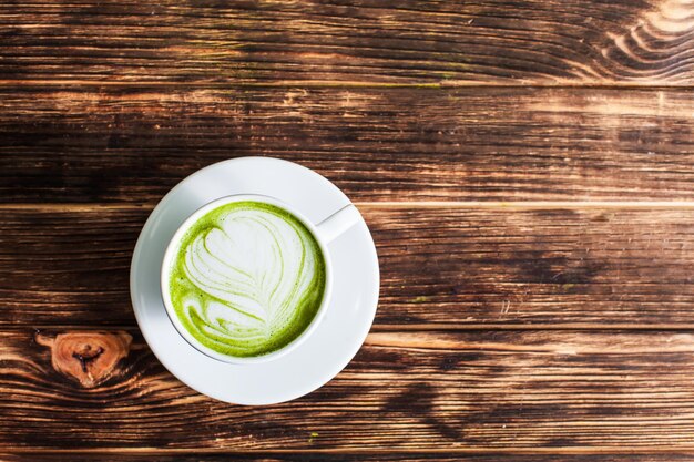 Draufsicht auf die Tasse Matcha Latte auf Holzuntergrund. Das Konzept des grünen Tees als Kunst