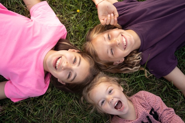 Draufsicht auf drei Mädchen, die lachen, während sie draußen auf dem Gras liegen, sorglos glückliches Kindheitskonzept