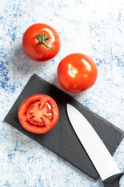 Draufsicht auf drei Tomaten, von denen eine neben einem Keramikmesser auf einem blauen Stein geschnitten wurde