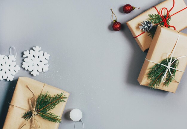 Draufsicht auf drei Weihnachtsgeschenke in einer mit Bändern verzierten Schachtel und einem Zweig eines Weihnachtsbaums auf grauem Hintergrund