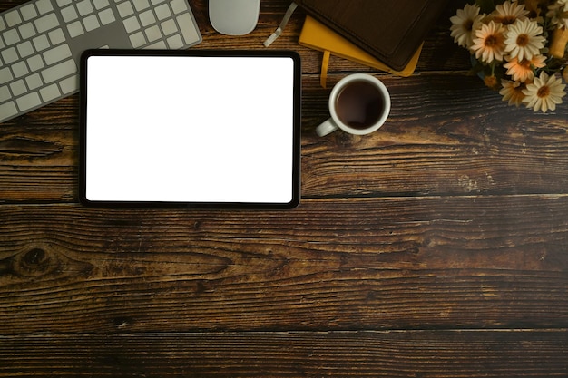 Draufsicht auf ein digitales Tablet mit kabelloser Tastatur, Kaffeetasse und Notizbüchern auf einem hölzernen Schreibtisch