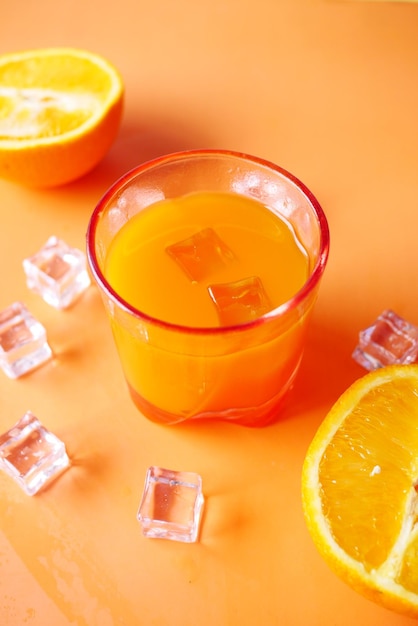 Draufsicht auf ein Glas Orangensaft mit Eis auf farbigem Hintergrund