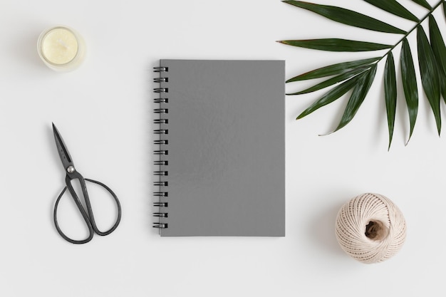 Draufsicht auf ein graues Notebook-Modell mit Arbeitsplatzzubehör und einem Palmblatt auf einem weißen Tisch