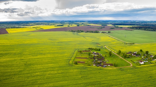 Draufsicht auf ein grünes Feld und ein kleines Dorf in Weißrussland. Landwirtschaftliche Felder im Dorf.