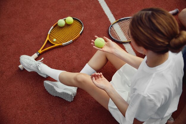 Foto draufsicht auf ein junges mädchen, das auf dem tennisplatz sitzt und den ball in der hand hält