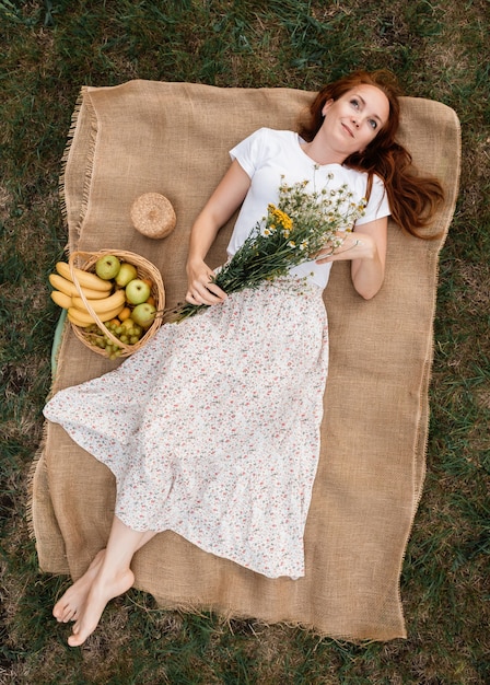 Draufsicht auf ein Mädchen in einem weißen Kleid mit einem Strauß Gänseblümchen und einem Obstkorb