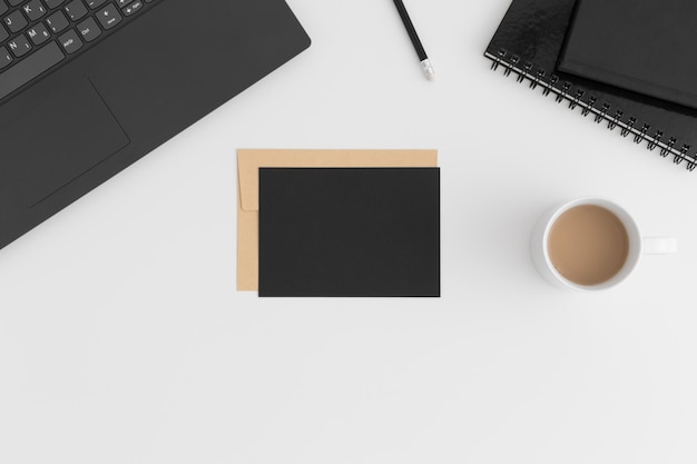 Draufsicht auf ein schwarzes Kartenmodell und einen Umschlag mit einer Laptoptasse Kaffee und Arbeitsplatzzubehör auf einem weißen Tisch