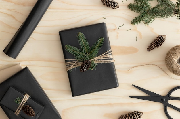 Draufsicht auf ein schwarzes Weihnachtsgeschenk, umgeben von Tannenzapfenblättern und Bindfäden auf einem Holztisch