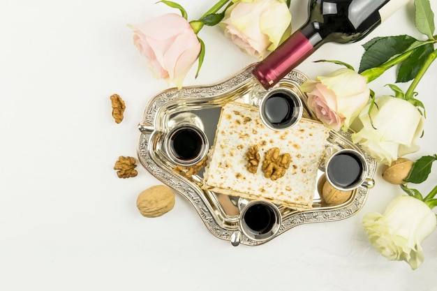 Draufsicht auf ein silbernes Tablett mit Matza, Walnüssen und Rotwein in silbernen Gläsern. Rosen auf weißem Hintergrund. das Konzept des jüdischen Pessach.