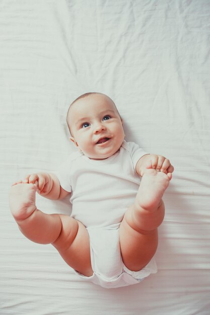 Draufsicht auf ein süßes Baby, das mit erhobenen Füßen auf einem Bett liegt