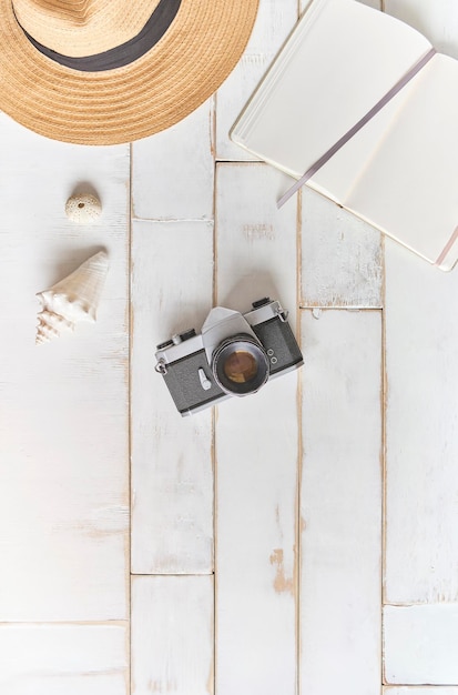 Draufsicht auf eine analoge Kamera und ein Notizbuch auf einem Holztisch. Die Hände des Fotografen halten eine alte Filmkamera auf einem hölzernen Hintergrund. Reise-Outfit-Konzept-Reise