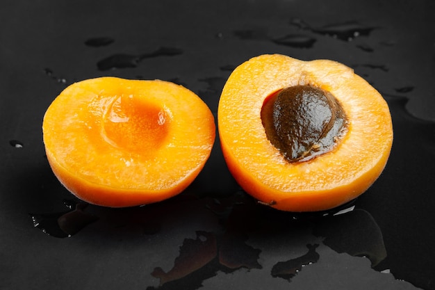 Draufsicht auf eine in Scheiben geschnittene nasse Aprikose auf einem nassen dunklen Hintergrund Frische saftige rötliche Aprikose auf einem dunklen