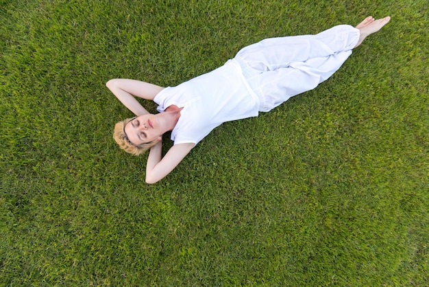 Draufsicht auf eine junge Frau, die sich im Gras entspannt, während sie mit den Händen hinter dem Kopf liegt, Entspannungs- und Naturkonzept