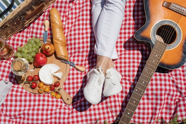 Draufsicht auf eine nicht wiederzuerkennende junge Frau in weißen Hosen, die draußen picknickt und Gitarre spielt