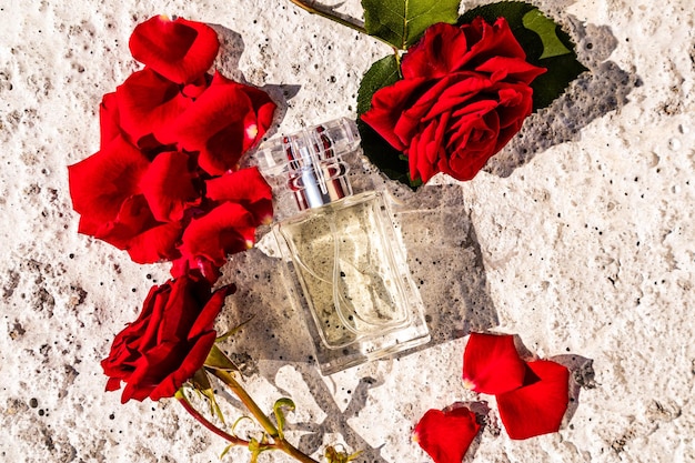 Draufsicht auf eine schicke Flasche Damenparfüm mit Rosenduft auf grauem Betongrund mit Blumen, die den Duft präsentieren