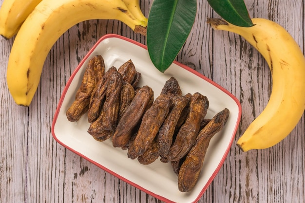 Draufsicht auf eine Schüssel mit getrockneten Bananen und frischen Bananen auf einem Holztisch Köstlicher natürlicher Fruchtsnack