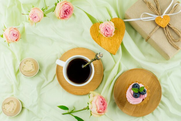 Draufsicht auf eine Tasse Kaffee, ein Herz aus Gold, ein Geschenk und Rosenknospen. pastellfarbener Hintergrund. das Konzept eines Valentinstags.