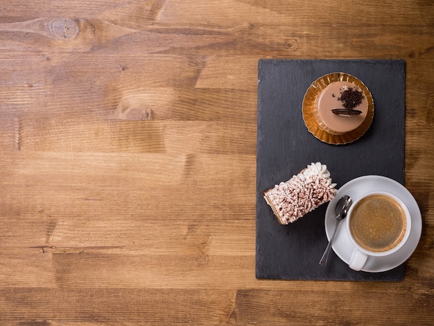 Draufsicht auf eine Tasse Kaffee in der Nähe von zwei verschiedenen Schokoladenkuchen auf Holztisch. Leckere Wüste. Köstlicher Kuchen. Frische Kuchen. Kopieren Sie Platz zur Verfügung.