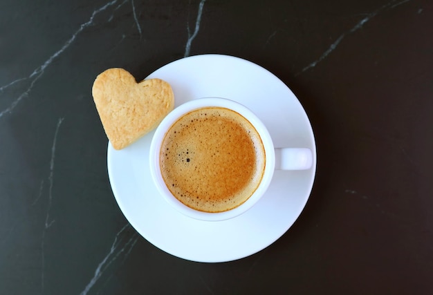 Draufsicht auf eine Tasse Kaffee mit herzförmigem Keks auf schwarzem Hintergrund