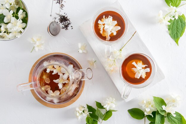 Draufsicht auf eine Teekanne aus Glas mit heilendem Jasmintee und zwei Glastassen Tee auf einem weißen Holzbrett trinken reich an Vitaminen und Mineralstoffen