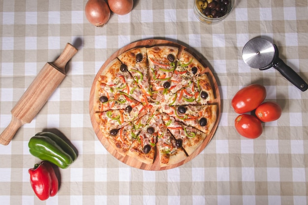 Draufsicht auf eine vegetarische Pizza mit verschiedenen Belägen auf einem karierten Tischtuch