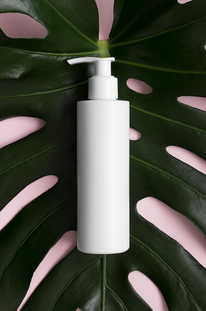 Draufsicht auf eine weiße Kosmetik-Shampoo-Spenderflasche mit einem Monstera-Blatt auf rosa Hintergrund