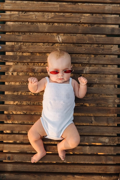 Draufsicht auf einen glücklichen kleinen Jungen mit Brille, der auf einer hölzernen Sonnenliege liegt