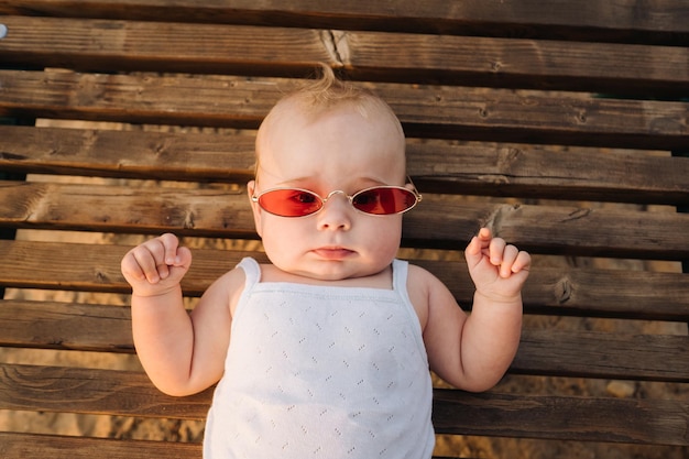 Draufsicht auf einen glücklichen kleinen Jungen mit Brille, der auf einer hölzernen Sonnenliege liegt