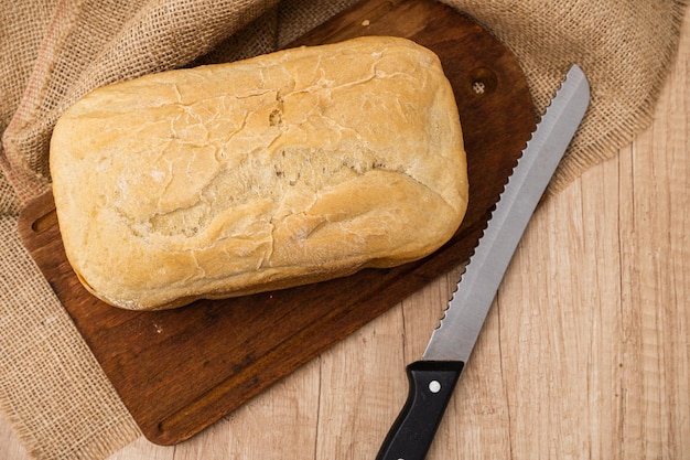 Draufsicht auf einen hausgemachten Brotlaib, der mit einer Brotmaschine auf einem Holzbrett mit einem Brotmesser hergestellt wurde Platz für Text