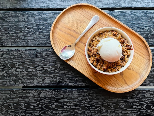 Draufsicht auf einen knusprigen Apfel-Pfirsich-Crumble mit weißem Eis auf dem Holztablett Roter kleiner Teller Backen Essen Essen Granola Nüsse Tisch Restaurant Kaffee Desserts Lecker Knusprig Knusprig