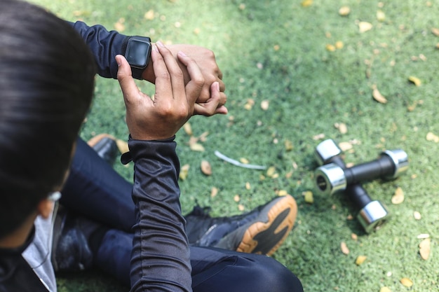 Draufsicht auf einen Mann in Sportkleidung, der auf die Smartwatch schaut und seinen Puls überprüft, während er im Park sitzt