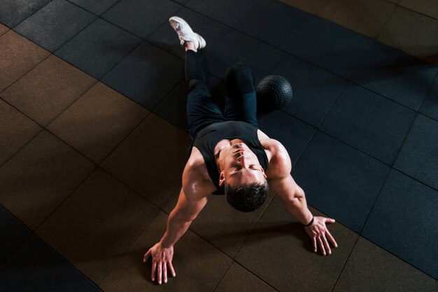 Draufsicht auf einen starken Mann in sportlicher Kleidung, der auf dem Boden sitzt und eine Pause im Fitnessstudio macht